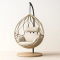 Sillón huevo colgante de ratán con cojines beige y base de madera para interiores